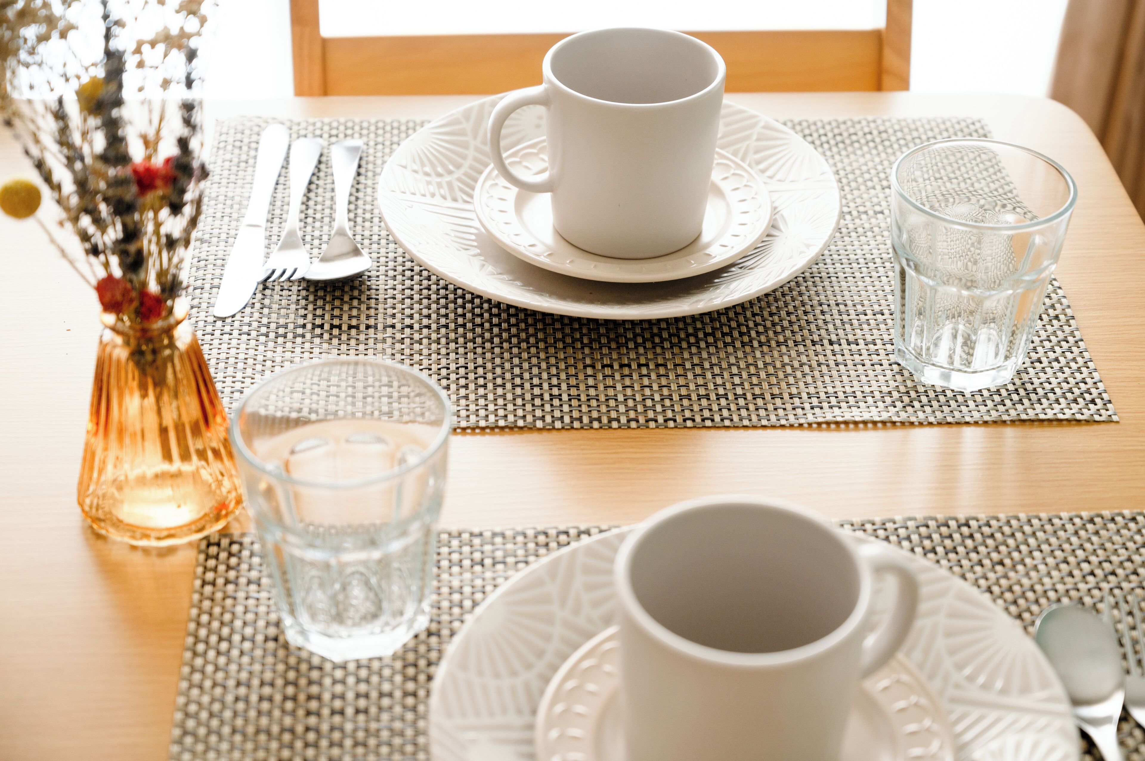 Une table à manger dressée avec des assiettes blanches, une tasse, des couverts et un verre.