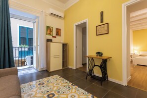 A living room with a patterned rug, a sewing machine table, and a bed in the adjacent room. - Cozy Mini Suite in a quiet neighborhood right in the heart of Palermo's historic center (Palermo)