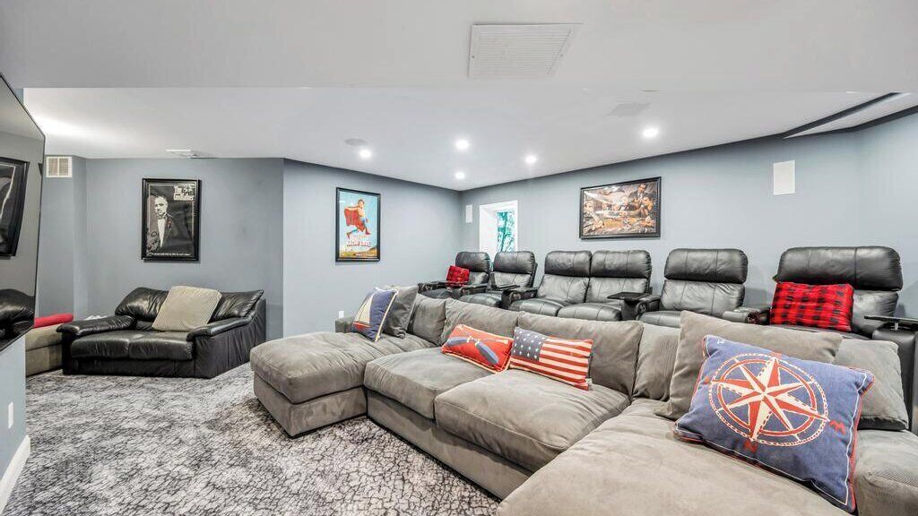 A home theater room with a sectional sofa, multiple recliner chairs, and a carpeted floor.