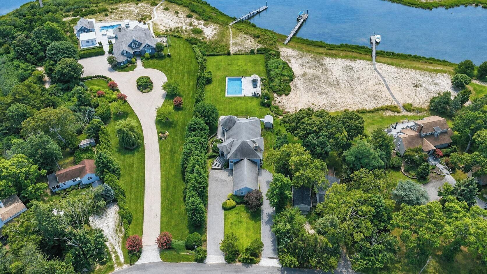 Vista aérea de uma área residencial com várias casas, uma piscina e um cais que se estende sobre a água.