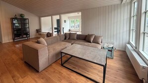 A spacious living room with a large L-shaped sectional sofa, a coffee table, and a wooden floor. - Wellness Center for 20 People—Spa, Sauna, and Activity Room (Hemmet)