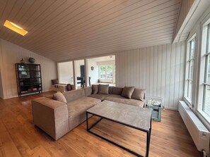 Ein geräumiges Wohnzimmer mit einer großen, im L-förmigen Grundriss angeordneten Couchgarnitur, einem Couchtisch und Holzboden.
