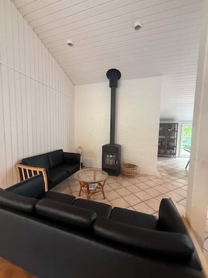 A cozy living area with a black sofa, a round glass table, and a wood-burning stove.