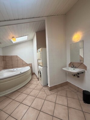 Et badeværelse med badekar, vask, spejl og vaskemaskine.