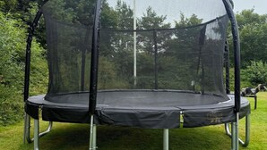A trampoline with a safety net enclosure, set on a grassy lawn. - Wellness Center for 20 People—Spa, Sauna, and Activity Room (Hemmet)