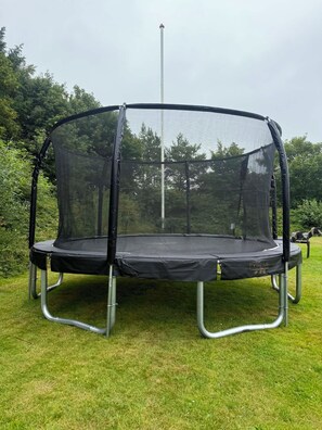 Ein Trampolin mit Sicherheitsnetz auf einer grünen Rasenfläche.
