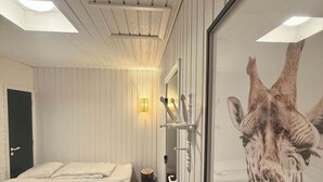 A hotel room with two beds, a wooden door, a wall-mounted lamp, and a giraffe poster. - Wellness Center for 20 People—Spa, Sauna, and Activity Room (Hemmet)