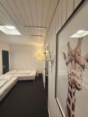 Ein Hotelzimmer mit zwei Betten, einer Holztür, einer Wandleuchte und einem Giraffenposter.