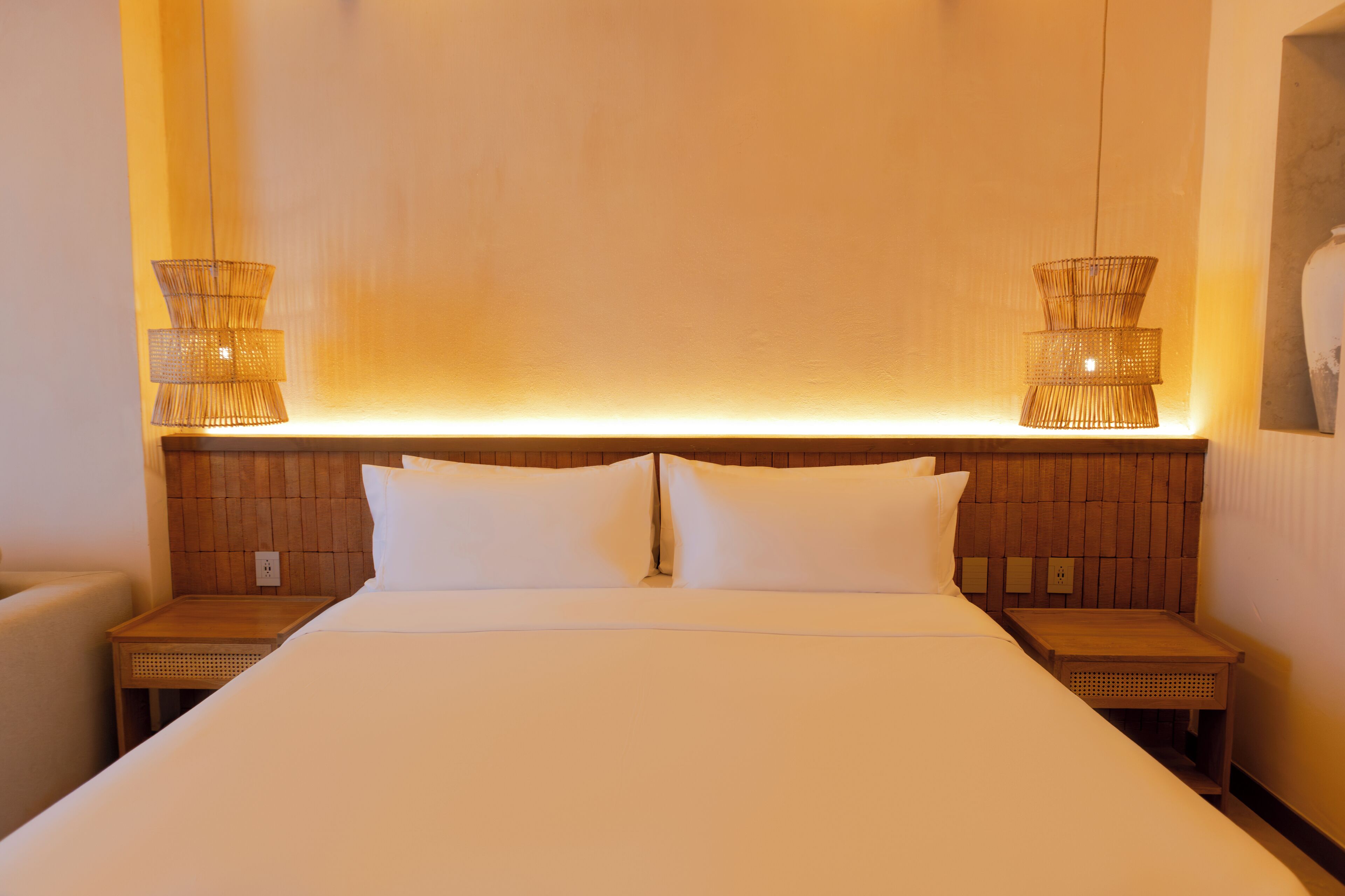 Habitación de hotel con una cama grande, dos mesitas de noche y una lámpara fijada a la pared.