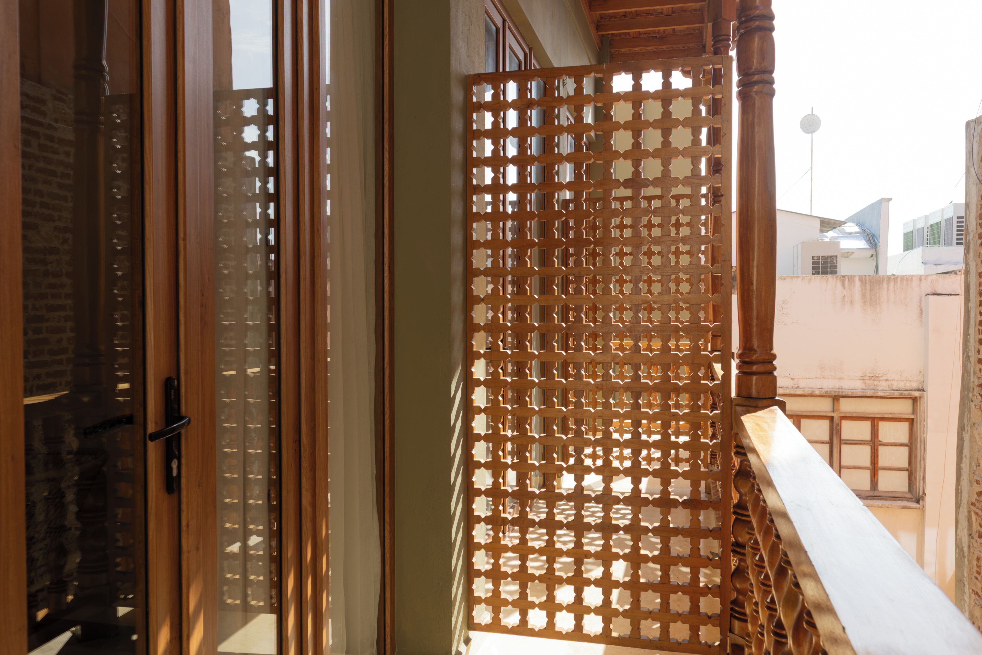 Guarda-corpo de madeira com design treliçado, porta de correr de vidro e vista dos edifícios ao redor.