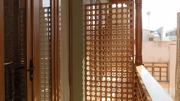 Guarda-corpo de madeira com design treliçado, porta de correr de vidro e vista dos edifícios ao redor.