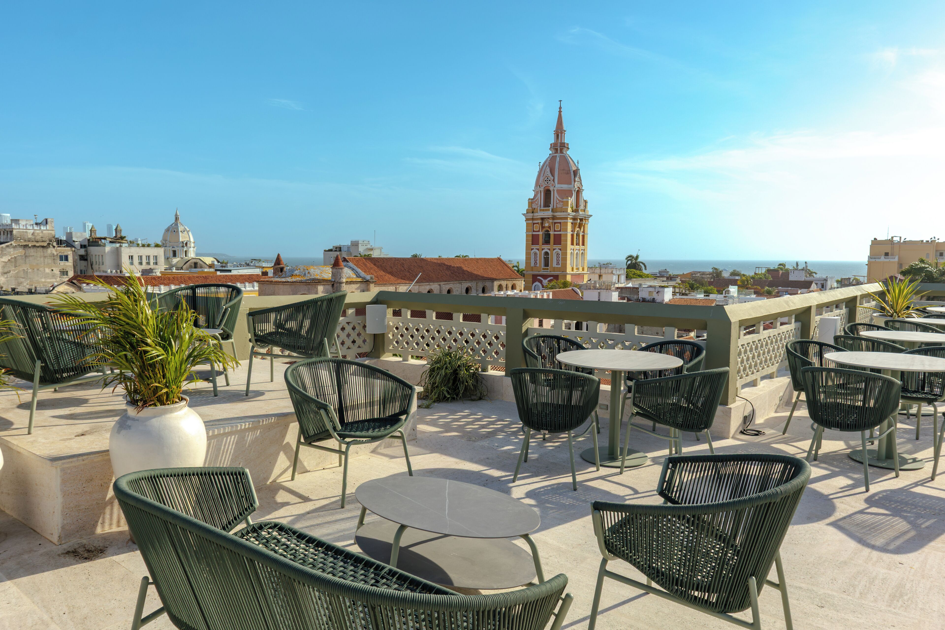 A rooftop terrace with outdoor seating, a view of a historic building, and a clear sky.