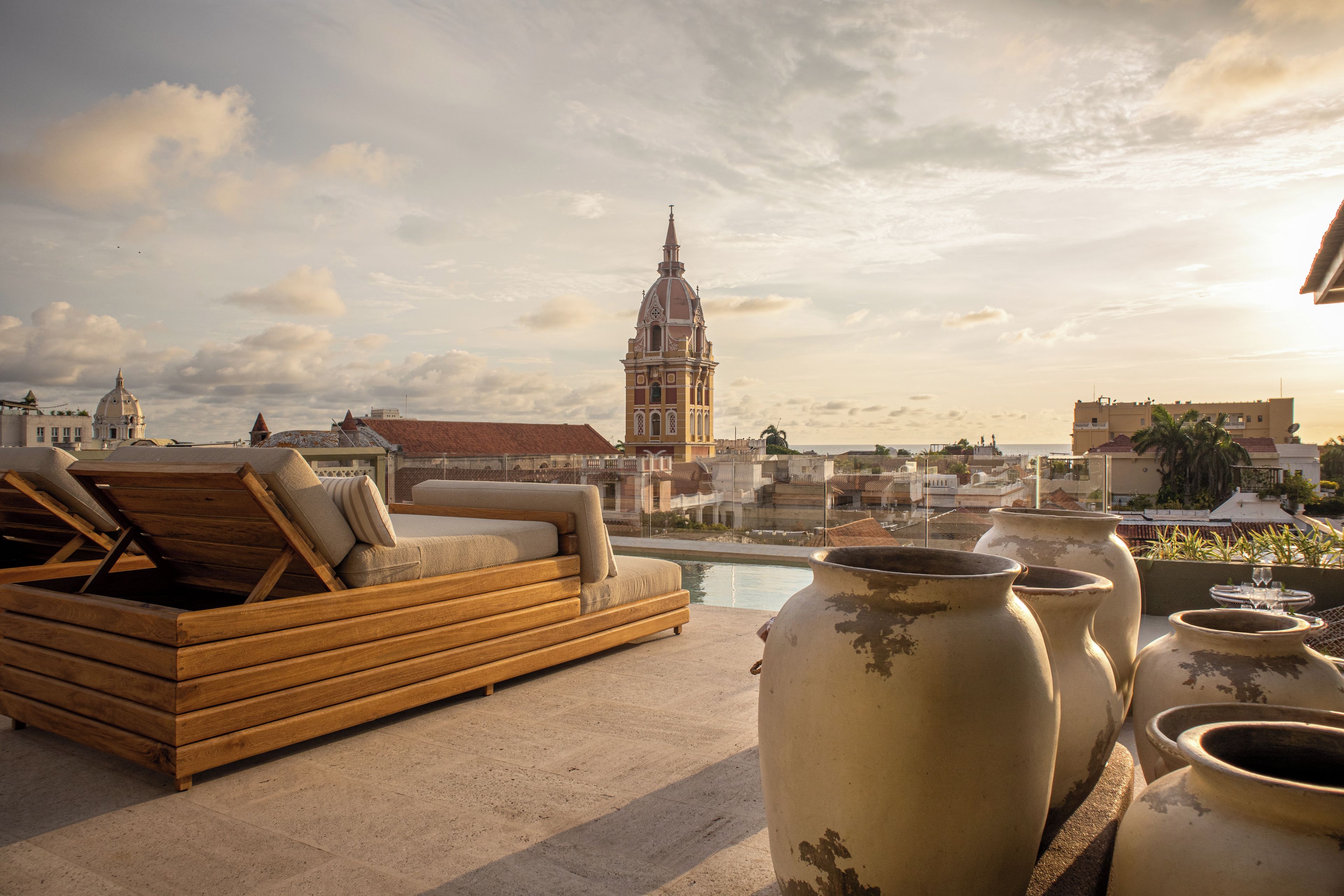 A rooftop terrace with a wooden lounge, a view of a historic church, and several large vases.