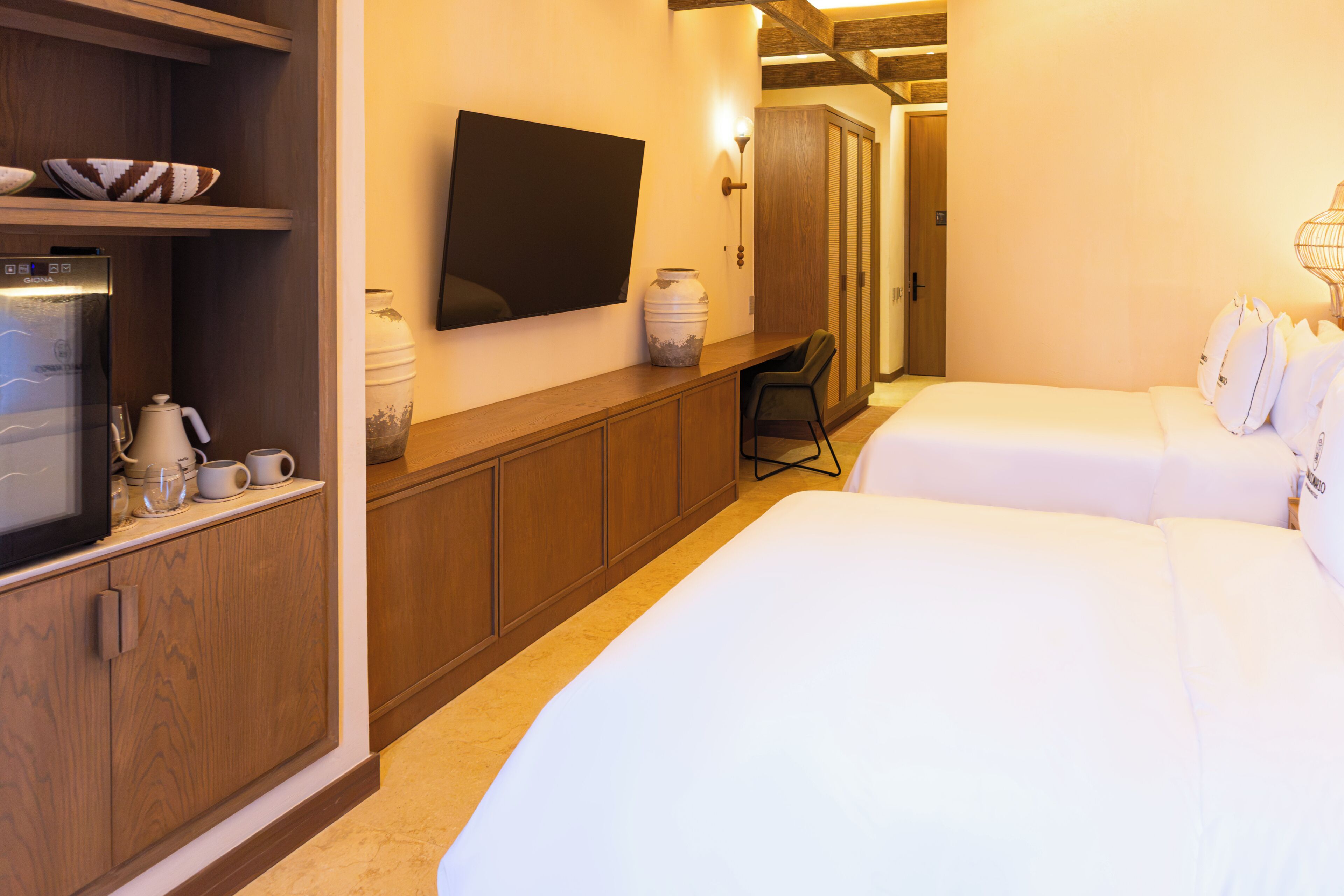 A hotel room with a bed, a desk with a chair, a television, and a minibar.