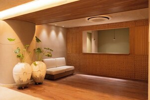 A modern interior with a wooden floor, a white sofa, and two large vases with plants.