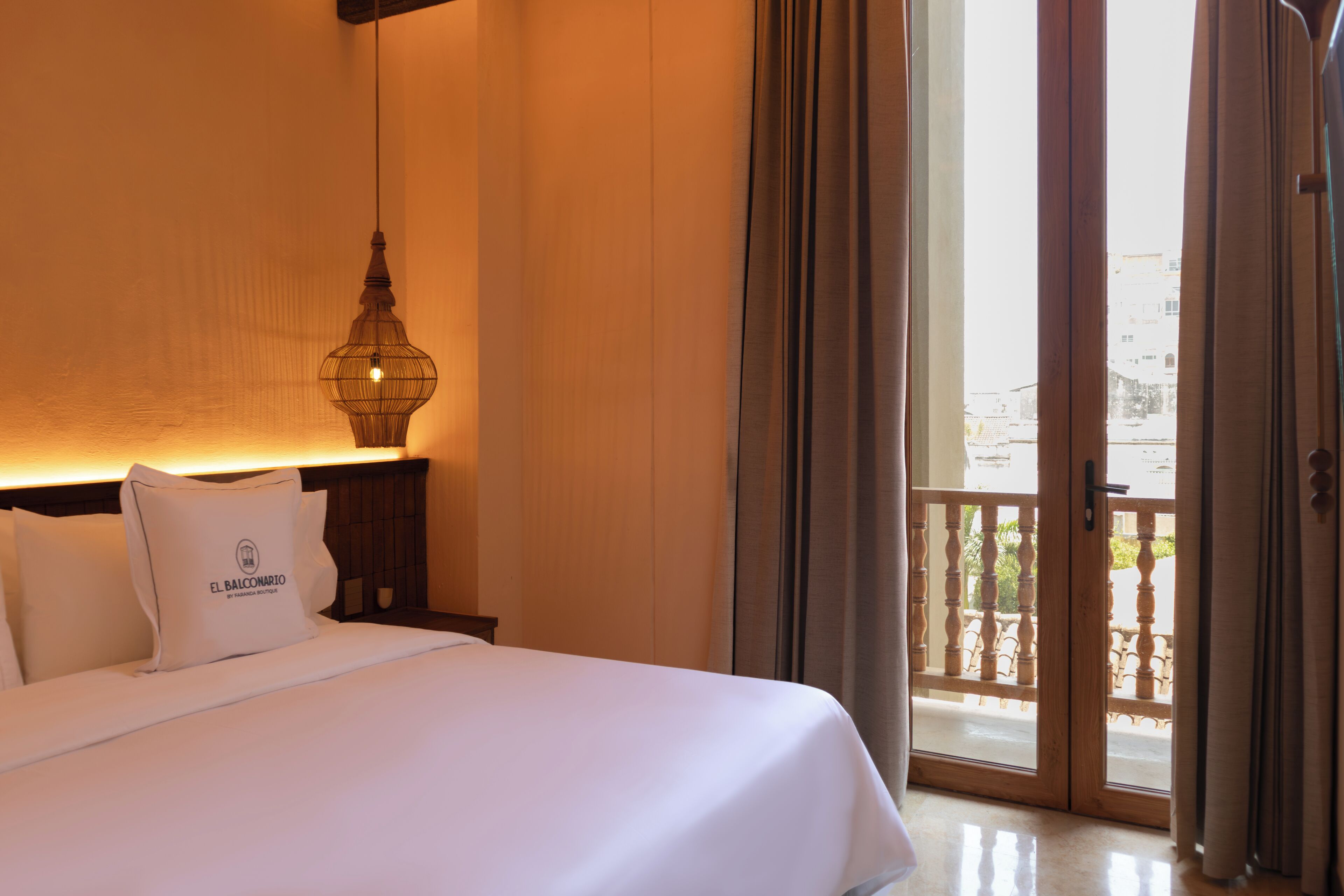 Une chambre d’hôtel avec un lit, une table de chevet avec une lampe et une vue sur l’extérieur, accessible par une porte-fenêtre donnant sur un balcon.
