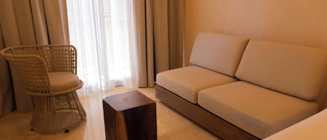 A room with a wicker chair, a wooden stool, and a sofa.