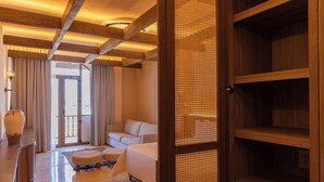 Une chambre d’hôtel comprenant un lit, un coin salon avec un canapé et un pouf, un bureau avec une lampe et une grande fenêtre.
