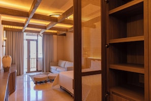 Et hotelværelse med seng, siddeområde med sofa og skænmøbel, skrivebord med lampe og et stort vindue.