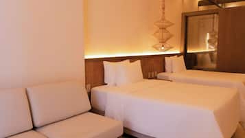 A hotel room with a sofa, two beds, a hanging light fixture, and a wooden headboard.