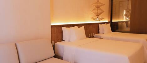 A hotel room with a sofa, two beds, a hanging light fixture, and a wooden headboard.