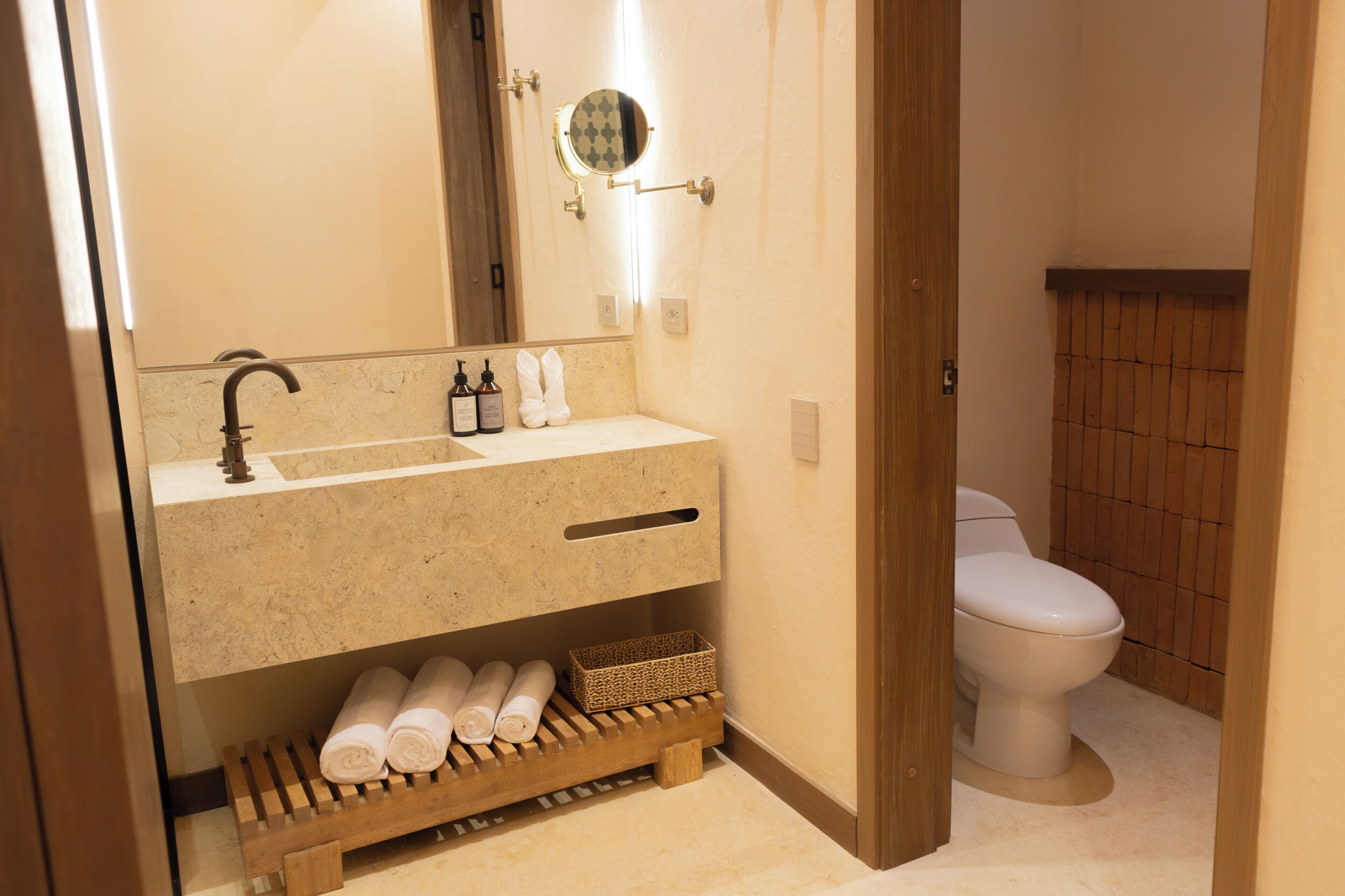A bathroom with a sink, mirror, toiletries, and a toilet.