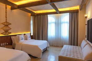 Una habitación de hotel con dos camas, un sofá, una lámpara colgante y un ventanal con cortinas.