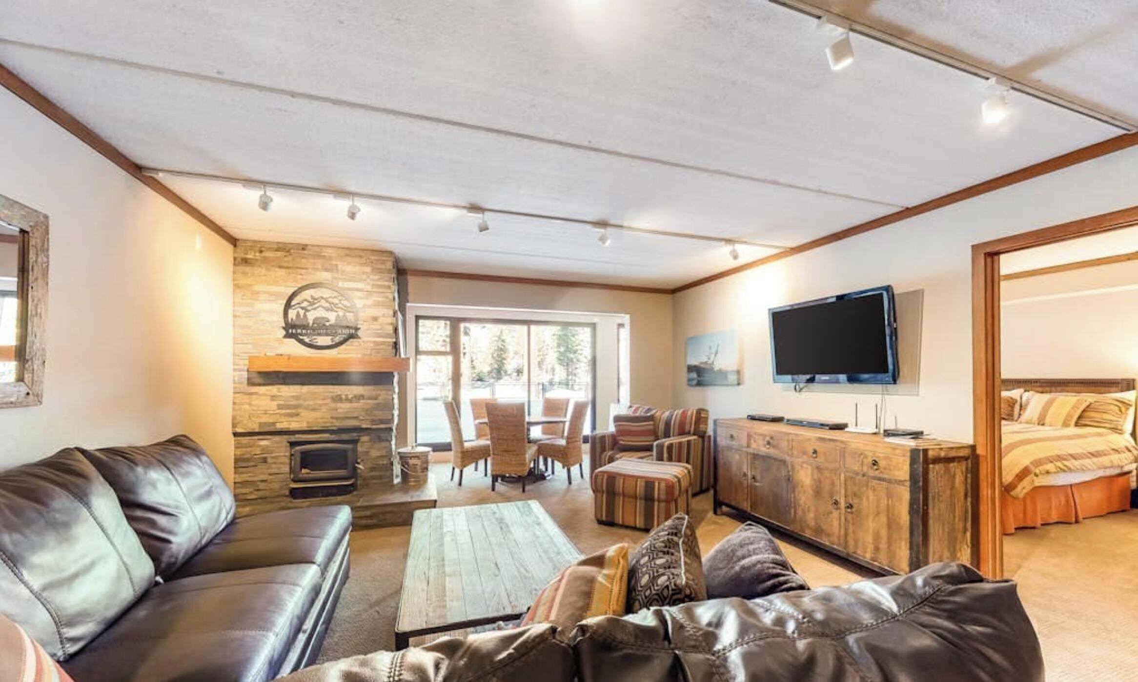 A spacious living room with leather sofas, a stone fireplace, and a television mounted on the wall.