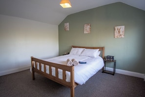 A bedroom with a wooden bed, a nightstand, and wall art. - Large Canalside Cottage | Games Room | Dog Walks (Loughborough)