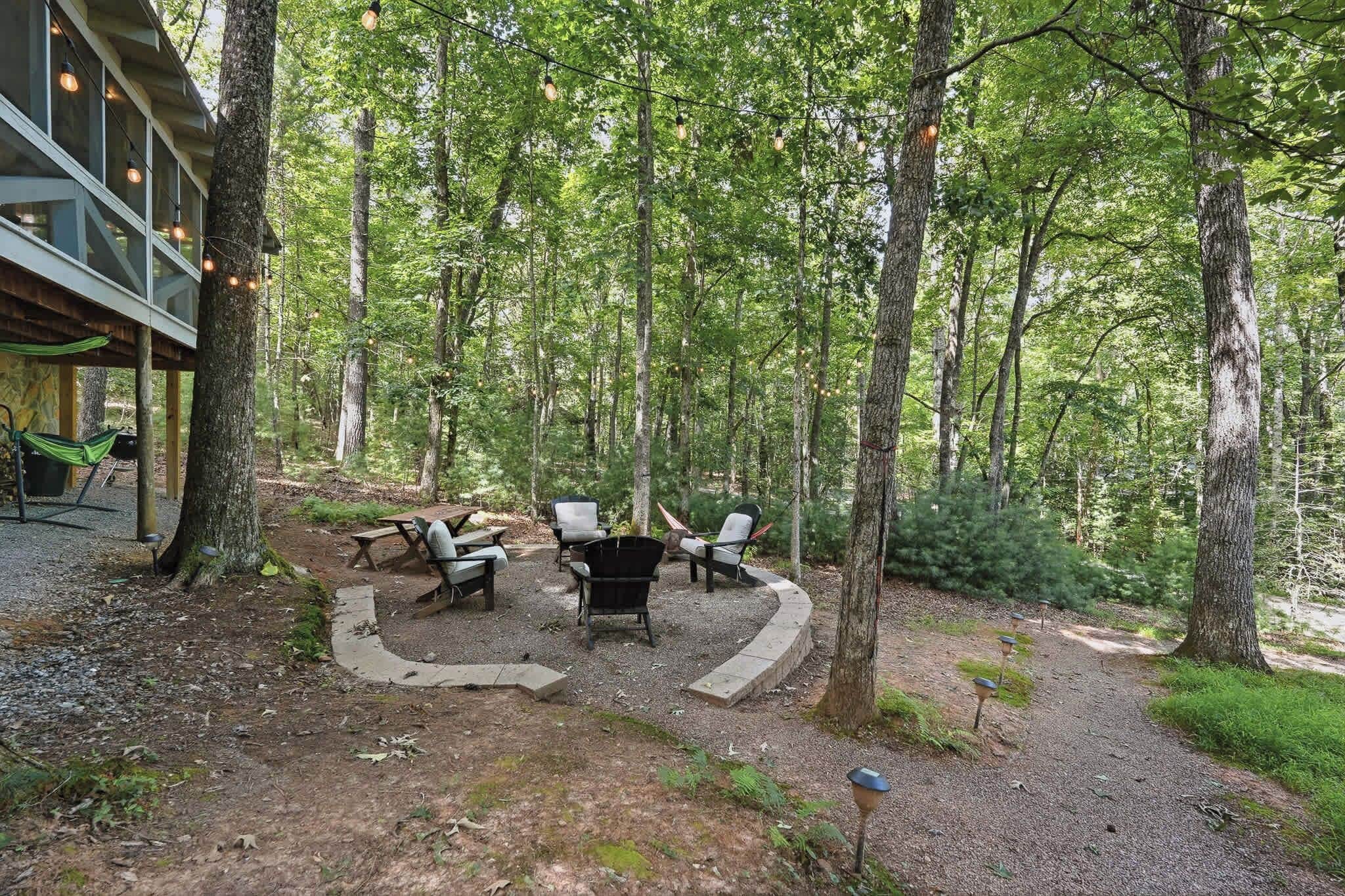 An outdoor seating area with a picnic table and chairs, surrounded by trees.