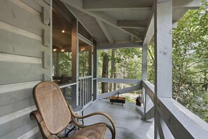 A wooden porch with a wicker chair and a bench, overlooking a forested area. - Peace of Aska - Hot Tub (Blue Ridge)
