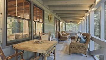 A covered porch with a wooden table and chairs, wicker furniture, and large windows.