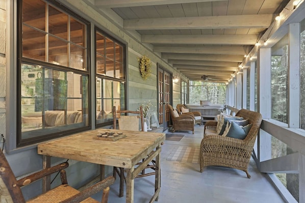 A covered porch with a wooden table and chairs, wicker furniture, and large windows. - Peace of Aska - Hot Tub (Blue Ridge)