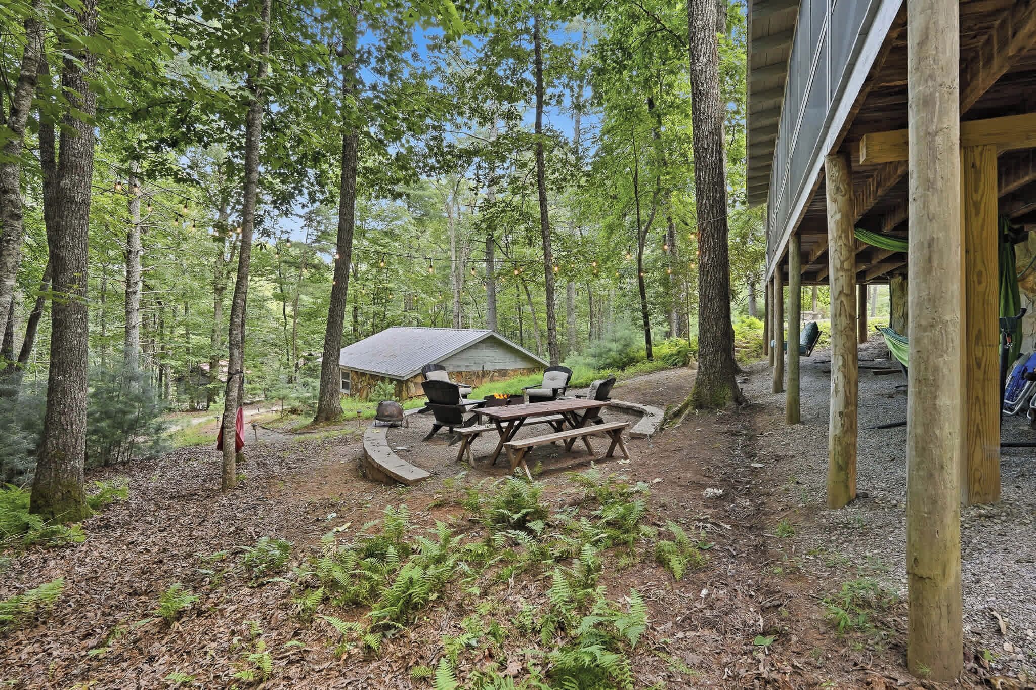 A rustic outdoor seating area with a fire pit and picnic table, surrounded by trees.