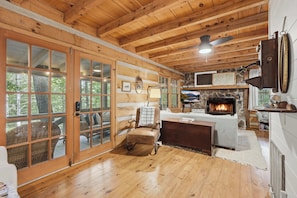 A cabin interior with a fireplace, wooden floors, and large windows. - Peace of Aska - Hot Tub (Blue Ridge)