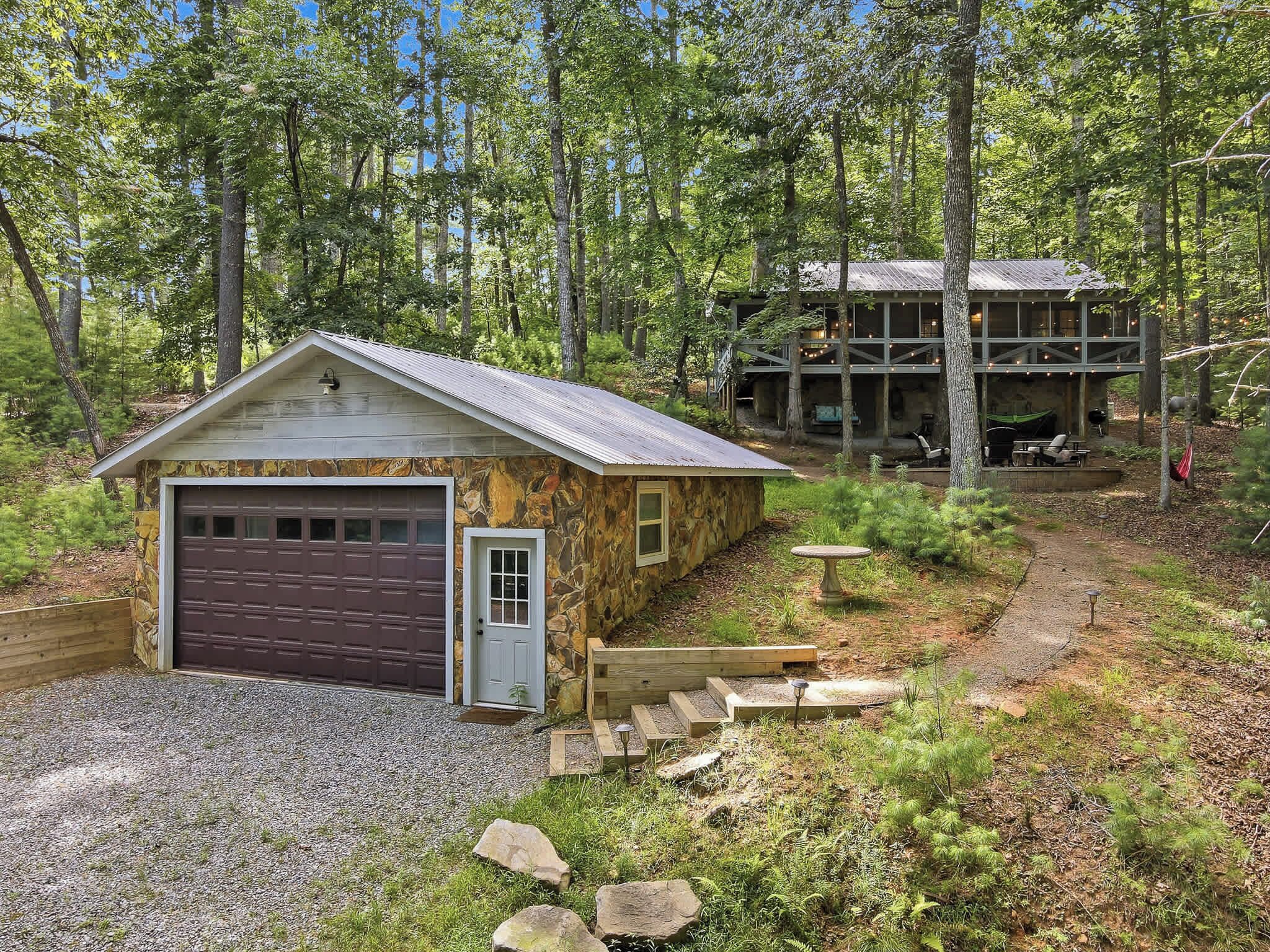 A rustic cabin with a garage, surrounded by a forest.