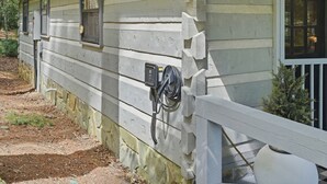 A rustic wooden house with a white exterior, a small window, and a power outlet on the side. - Peace of Aska - Hot Tub (Blue Ridge)