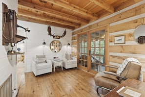 A log cabin interior with a wooden ceiling, white walls, a round mirror, a fireplace, and a large window. - Peace of Aska - Hot Tub (Blue Ridge)