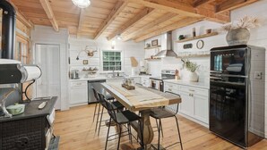 A kitchen with a central island, wooden beams, white cabinetry, and a black refrigerator. - Peace of Aska - Hot Tub (Blue Ridge)
