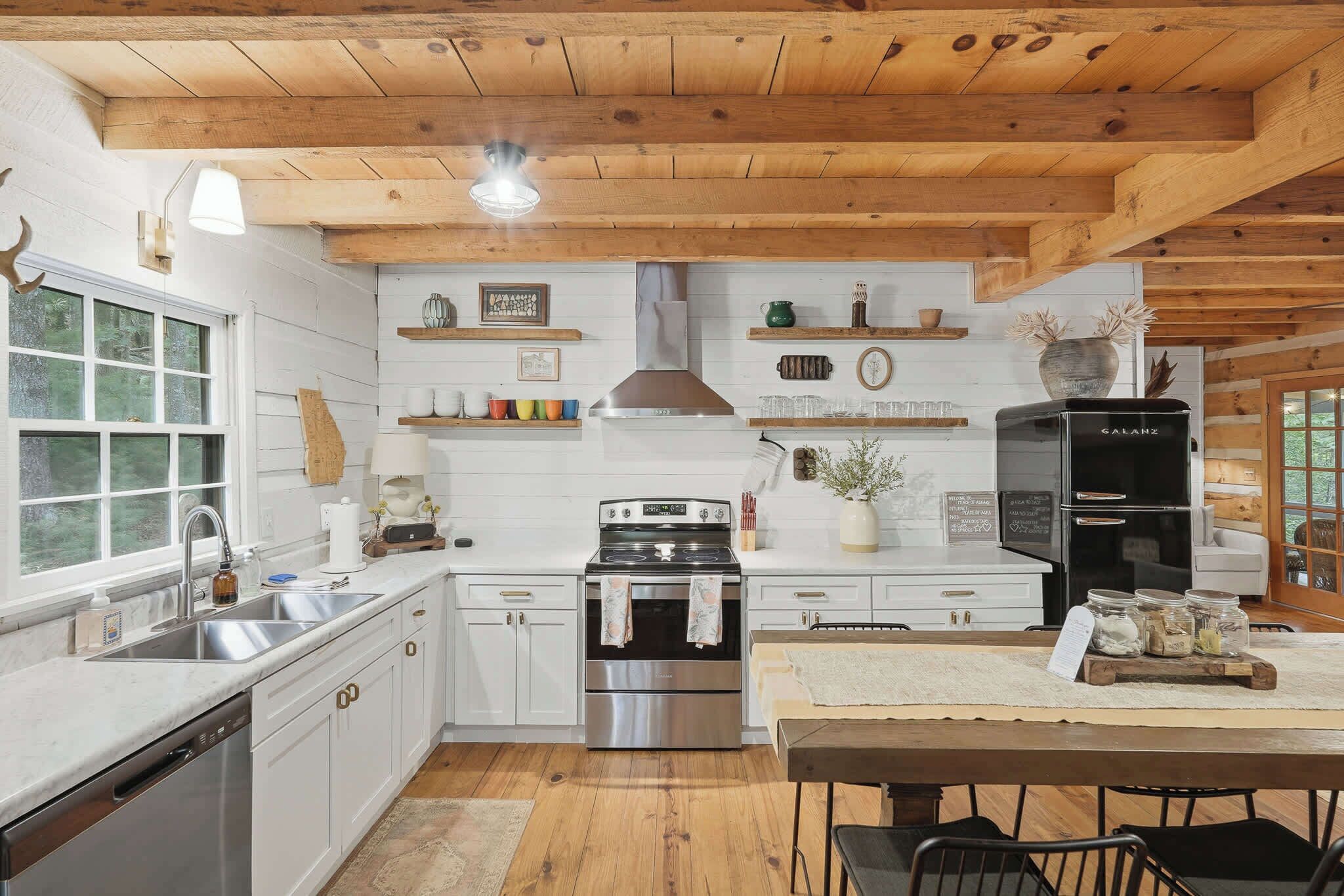 A kitchen with white cabinets, stainless steel appliances, wooden beams, and a black refrigerator.
