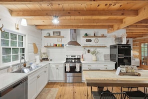 A kitchen with white cabinets, stainless steel appliances, wooden beams, and a black refrigerator. - Peace of Aska - Hot Tub (Blue Ridge)