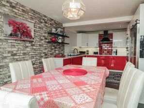 Una cocina moderna con armarios rojo y blanco, una pared de acento de ladrillo y un comedor con mantel rojo.