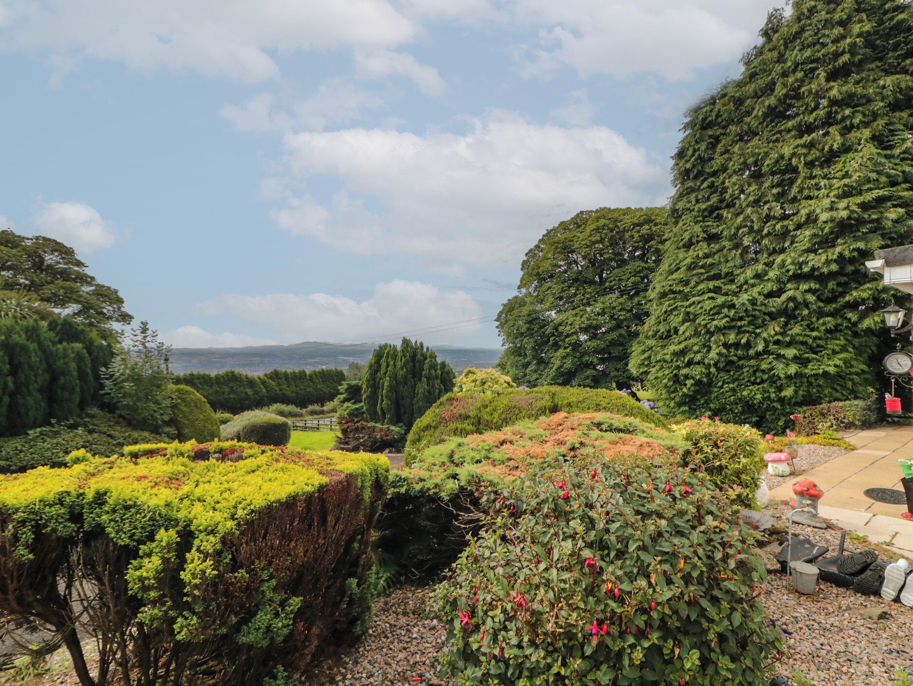 A landscaped garden with various plants and trees, a pathway, and a distant view of the landscape.