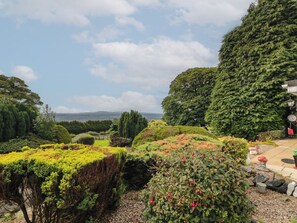 A landscaped garden with various plants and trees, a pathway, and a distant view of the landscape.