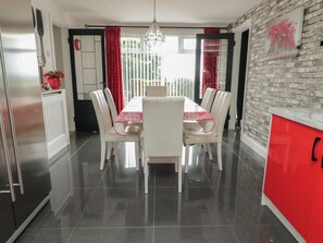 Un comedor con una mesa y sillas blancas, un armario rojo y una cocina con refrigerador.