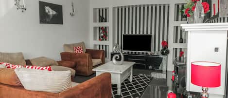 A modern living room with a sofa, armchairs, a coffee table, a flat-screen TV, and decorative items.