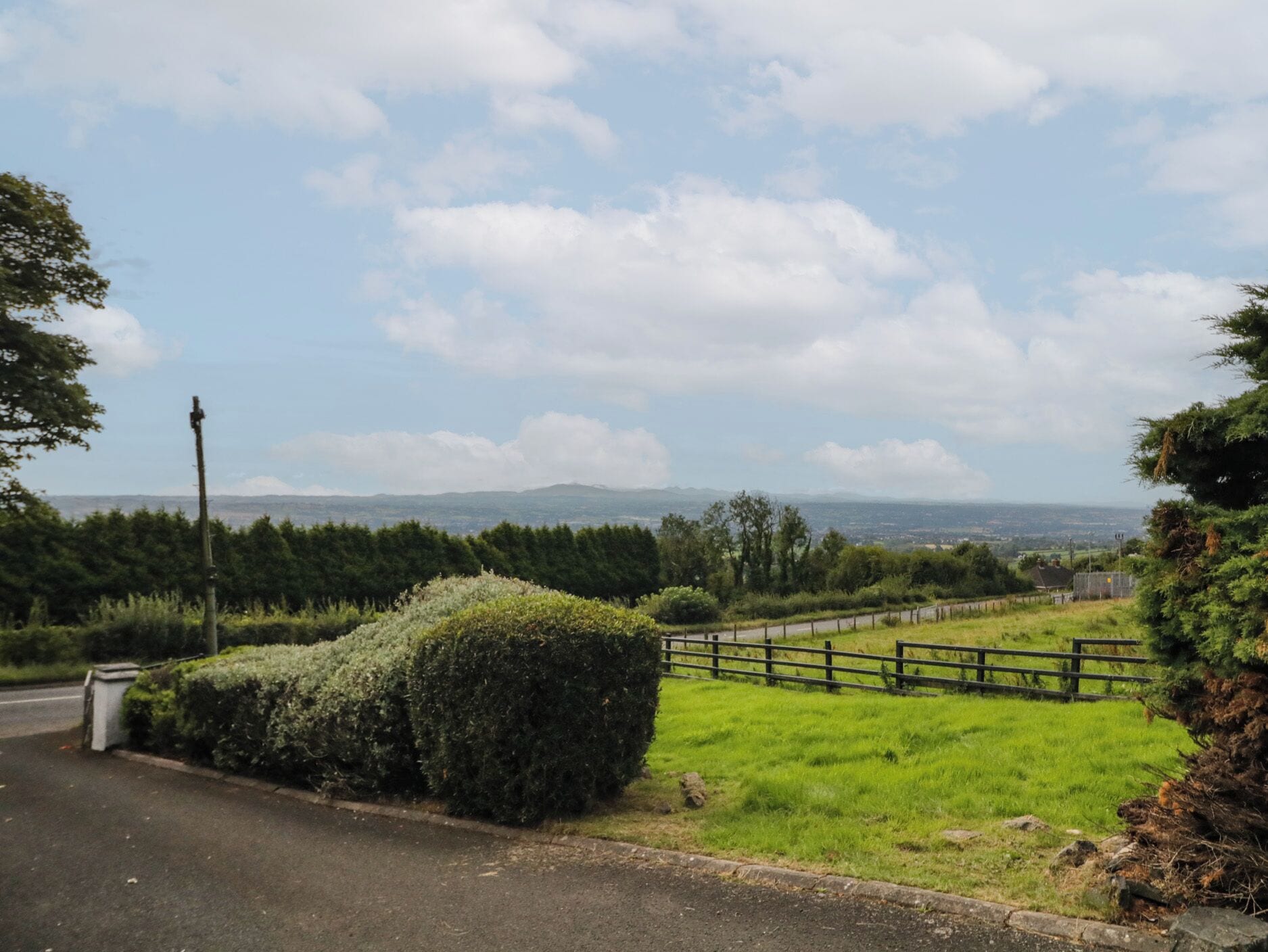 A rural road with a hedge and a wooden fence.