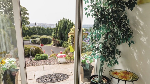 Vista a través de un ventanal hacia un jardín con una planta en maceta, una mesa decorativa y una pequeña mesa con diseño floral.