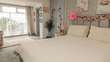 A bedroom with a large bed, a nightstand, a lamp, and a window with curtains.