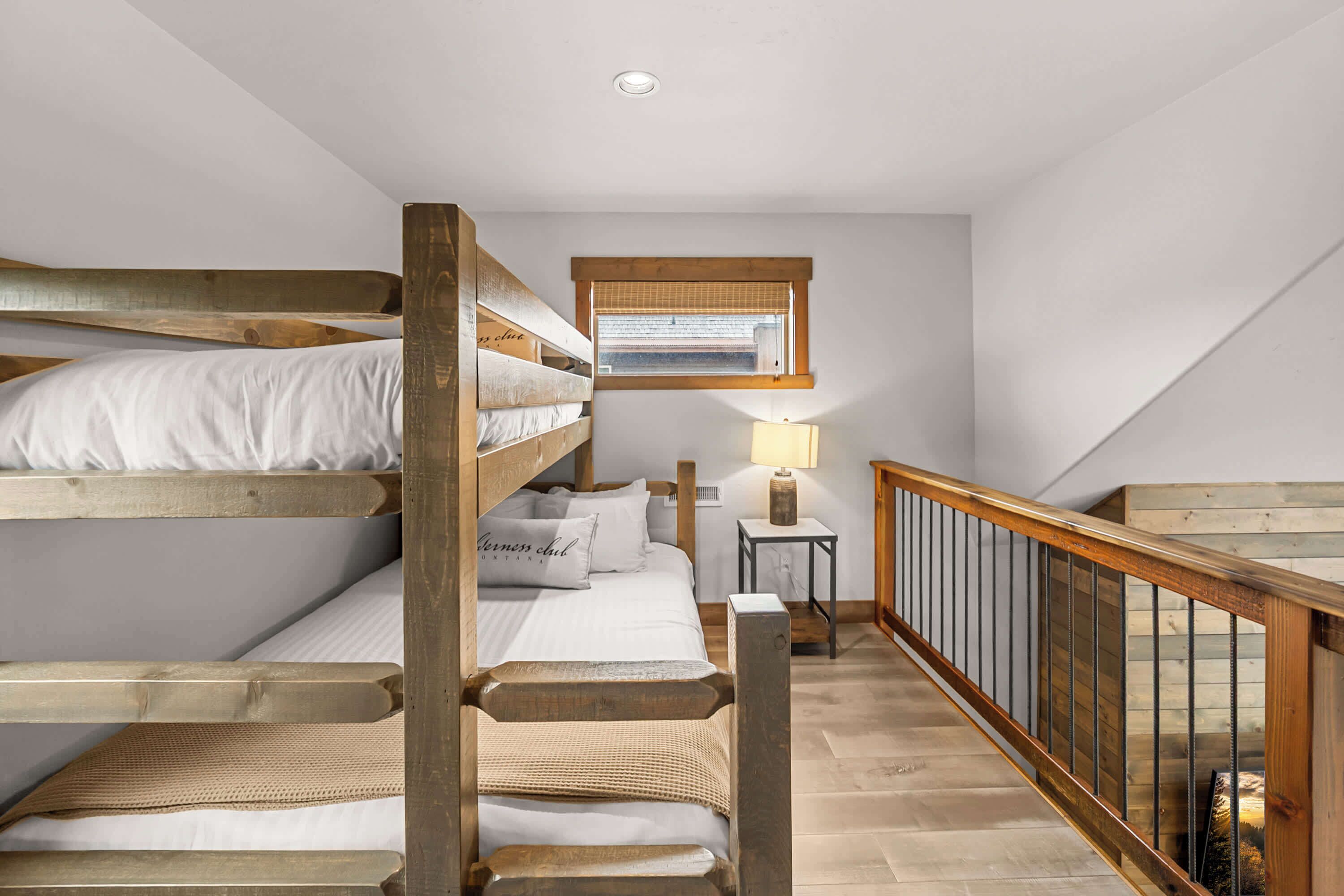 A dormitory-style room with bunk beds, a small desk with a lamp, and a window with blinds.
